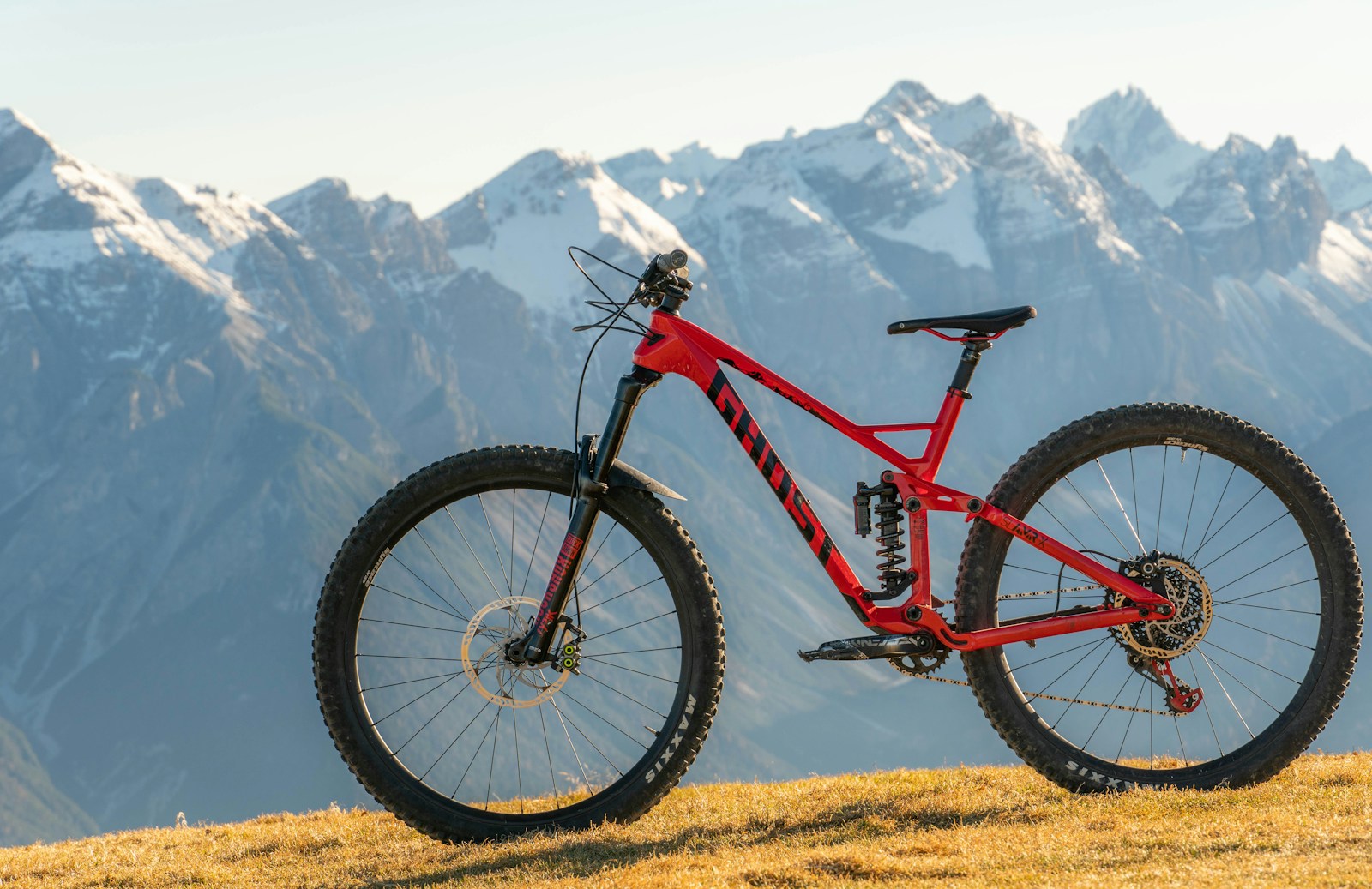Red mountain bike resting on a grassy hilltop.