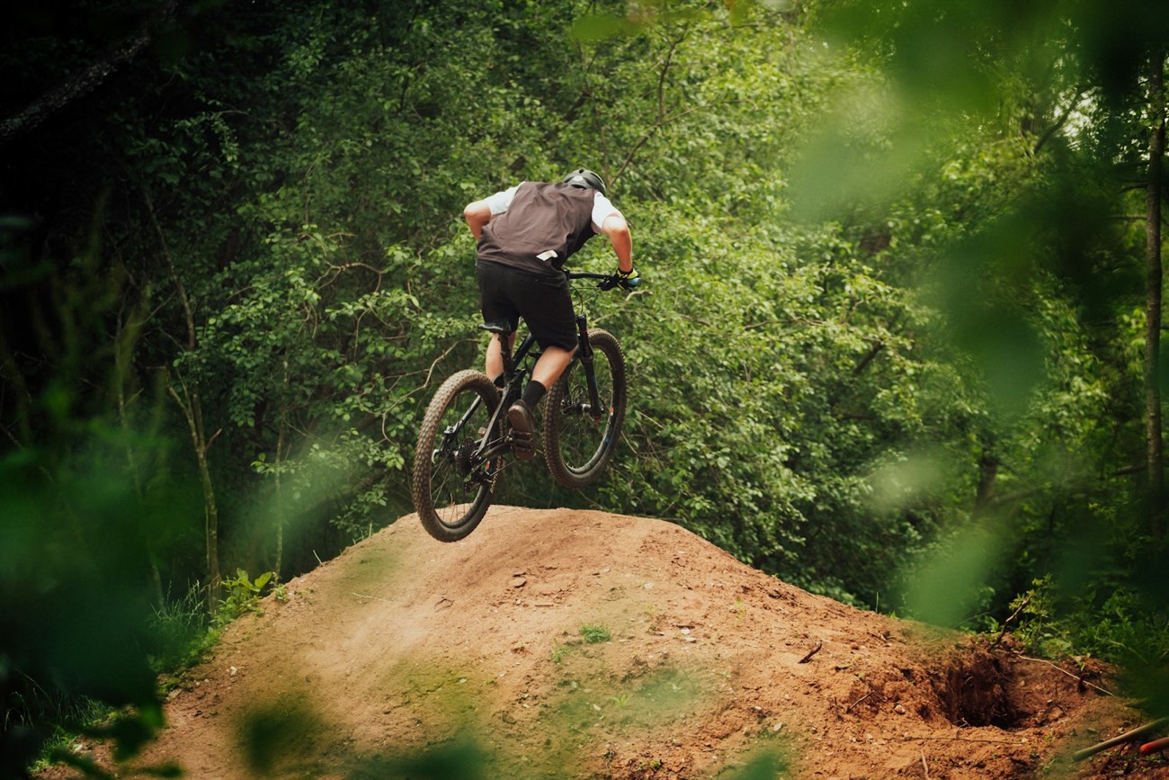 Mountain biker riding through a green forested trail.